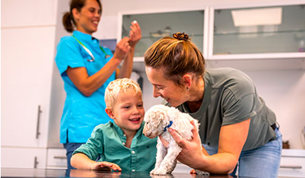 Woman and child smile with a dog in a veterinary clinic as a member of the veterinary staff prepares a vaccine