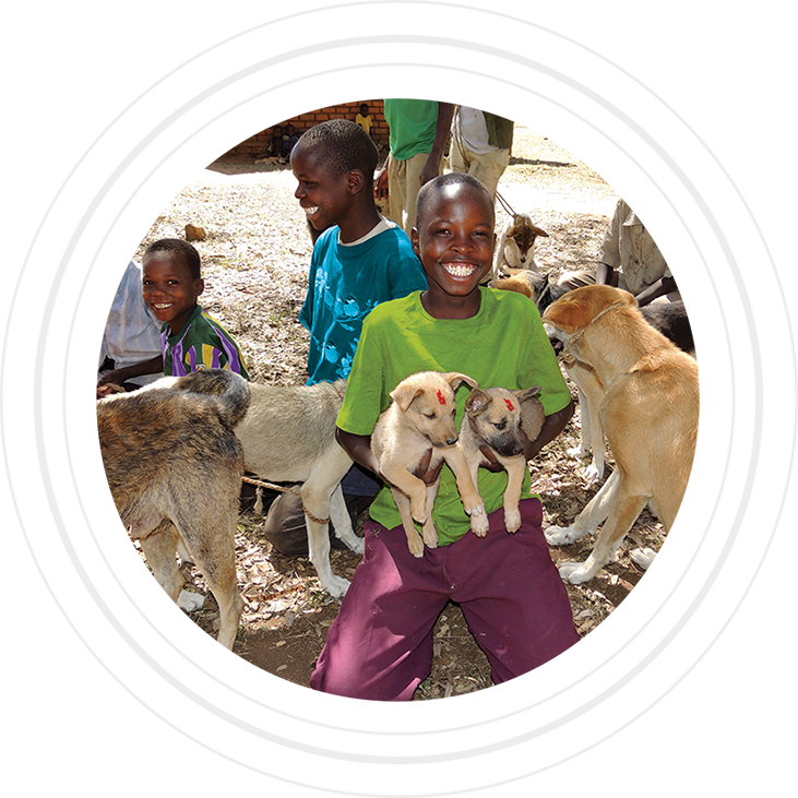 Smiling child holds two puppies in the center of a group of dogs and children